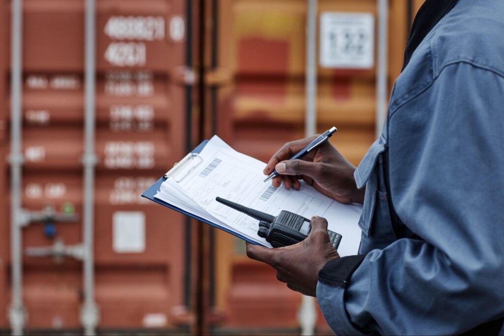 person checking shipping documents on clipboard near cargo containers